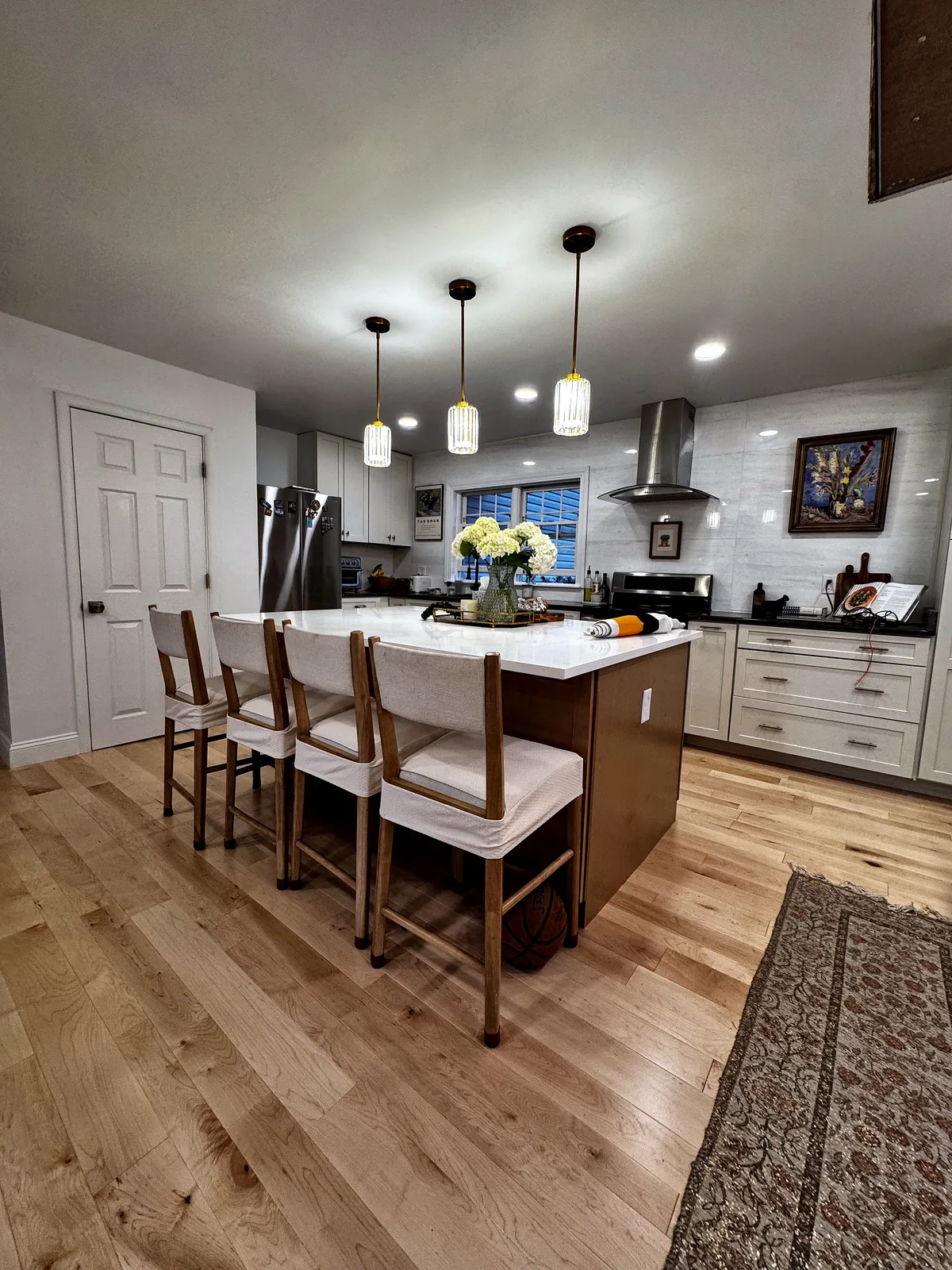 Finished kitchen island with white cabinets, pendant lights, hardwood flooring, and dark countertops